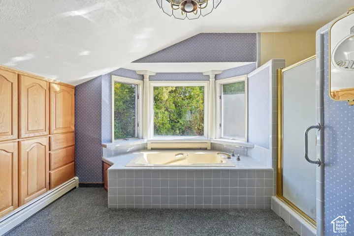 Built-in storage cabinetry, bay window, tiled soaking tub, tiled shower with gold-toned frame, and ceiling-mounted light fixture