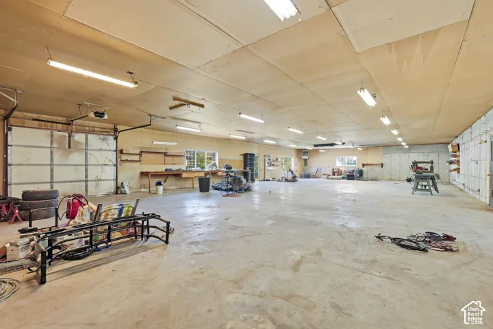 Spacious interior featuring a large garage door, concrete flooring, exposed ceiling, built-in shelving, and multiple windows