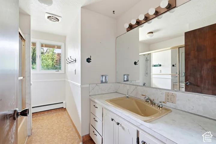 Vanity with integrated sink, full-width mirror with overhead lighting, white cabinetry with decorative pulls, and a window with exterior views