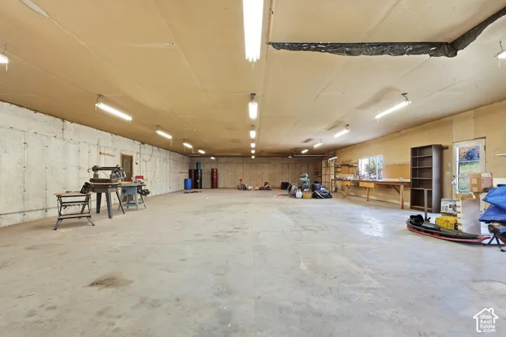 Expansive concrete floor, concrete walls, multiple fluorescent light fixtures, and a workbench with shelving