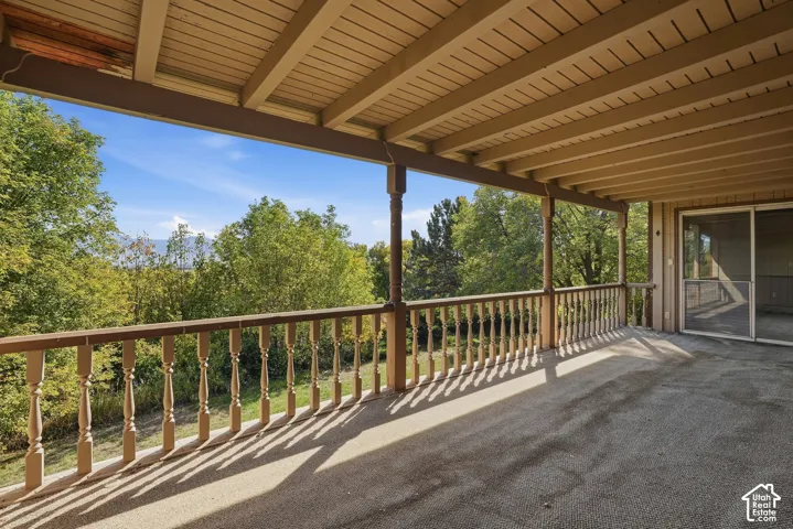Expansive covered deck featuring a textured surface, classic baluster railings, and a sliding glass door entry