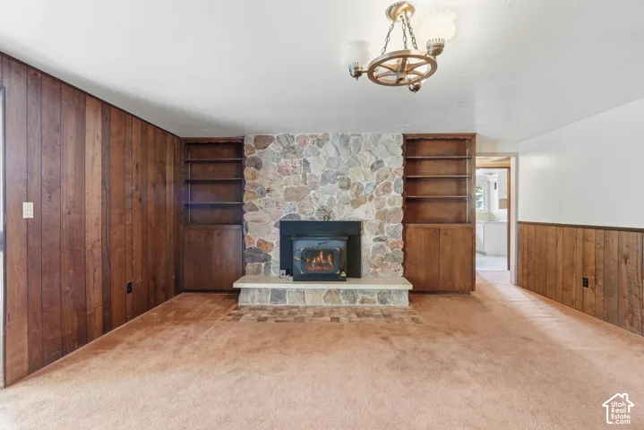 Stone fireplace with a hearth, integrated wood-finish shelving, wood-finish paneling, and a decorative chandelier