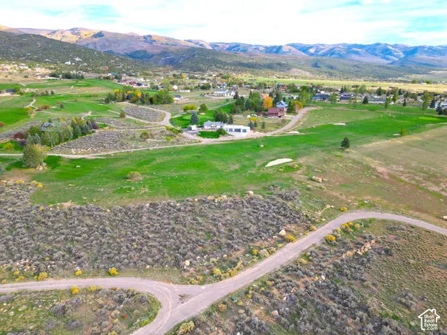 Expansive green landscape with distant mountains, featuring a golf course, residential structures, and winding roads