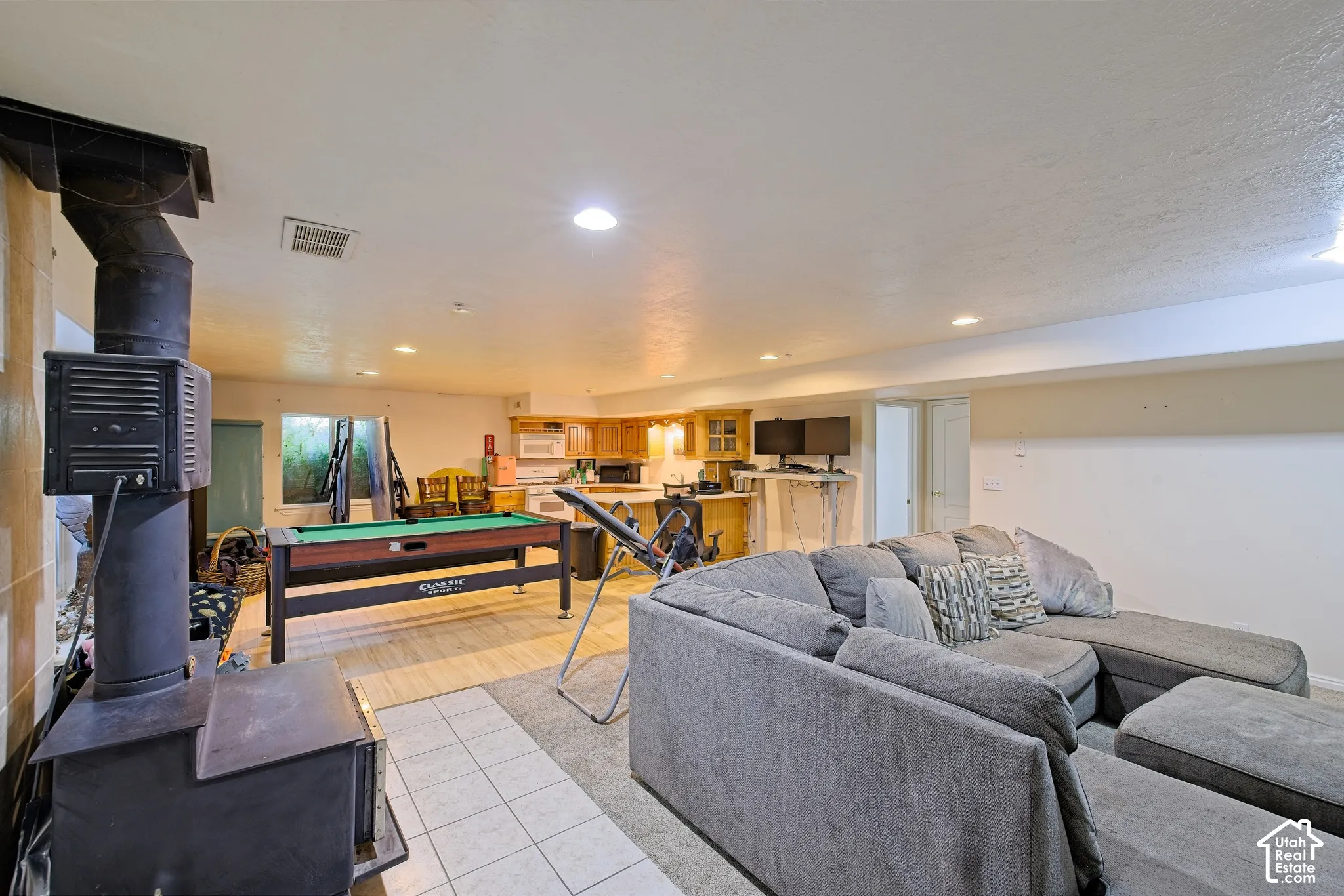 Open-concept living space with a wood-burning stove, recessed lighting, and a kitchen area featuring wood-finish cabinetry