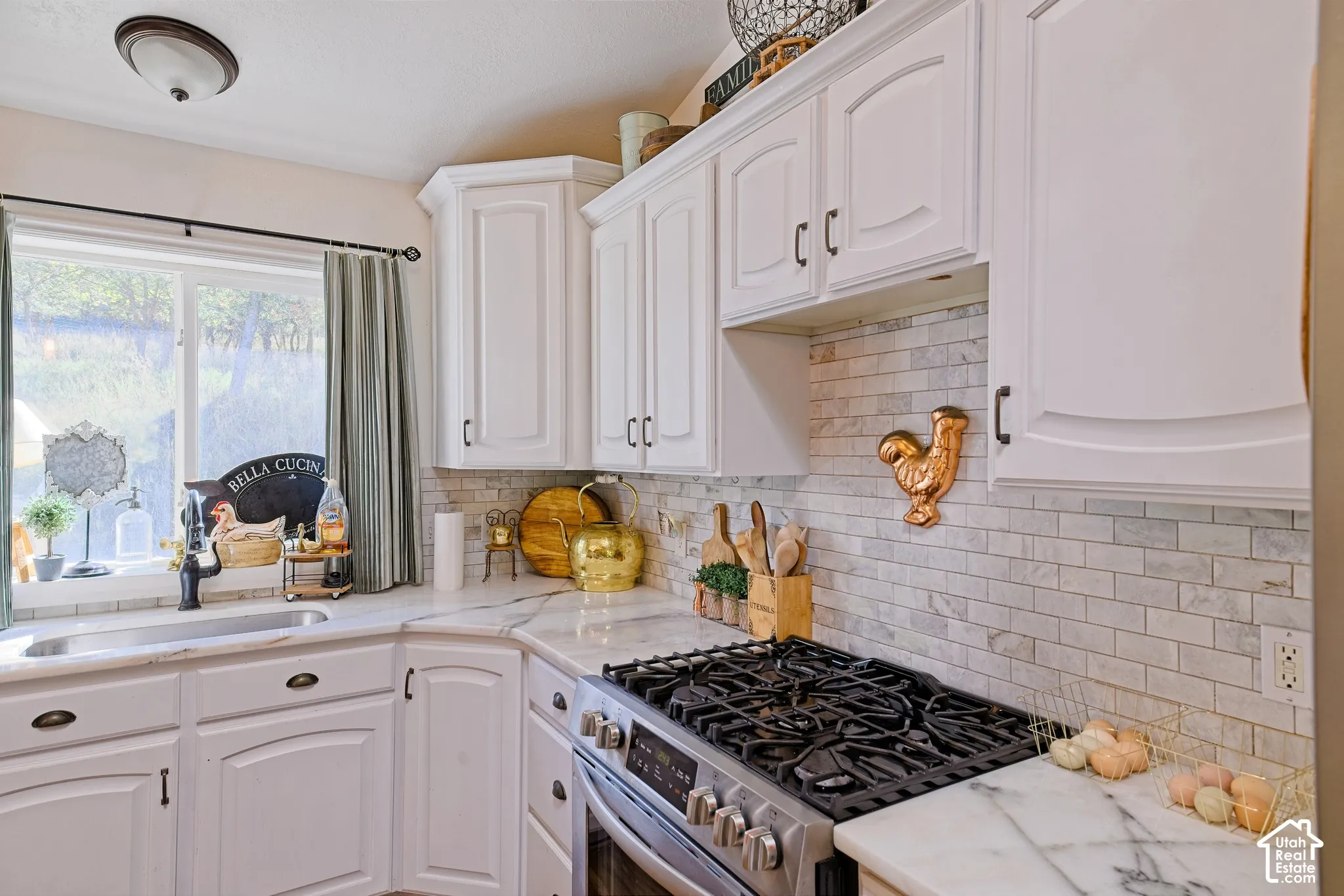 White cabinetry with dark hardware, stone countertops, stainless steel range, and a tiled backsplash