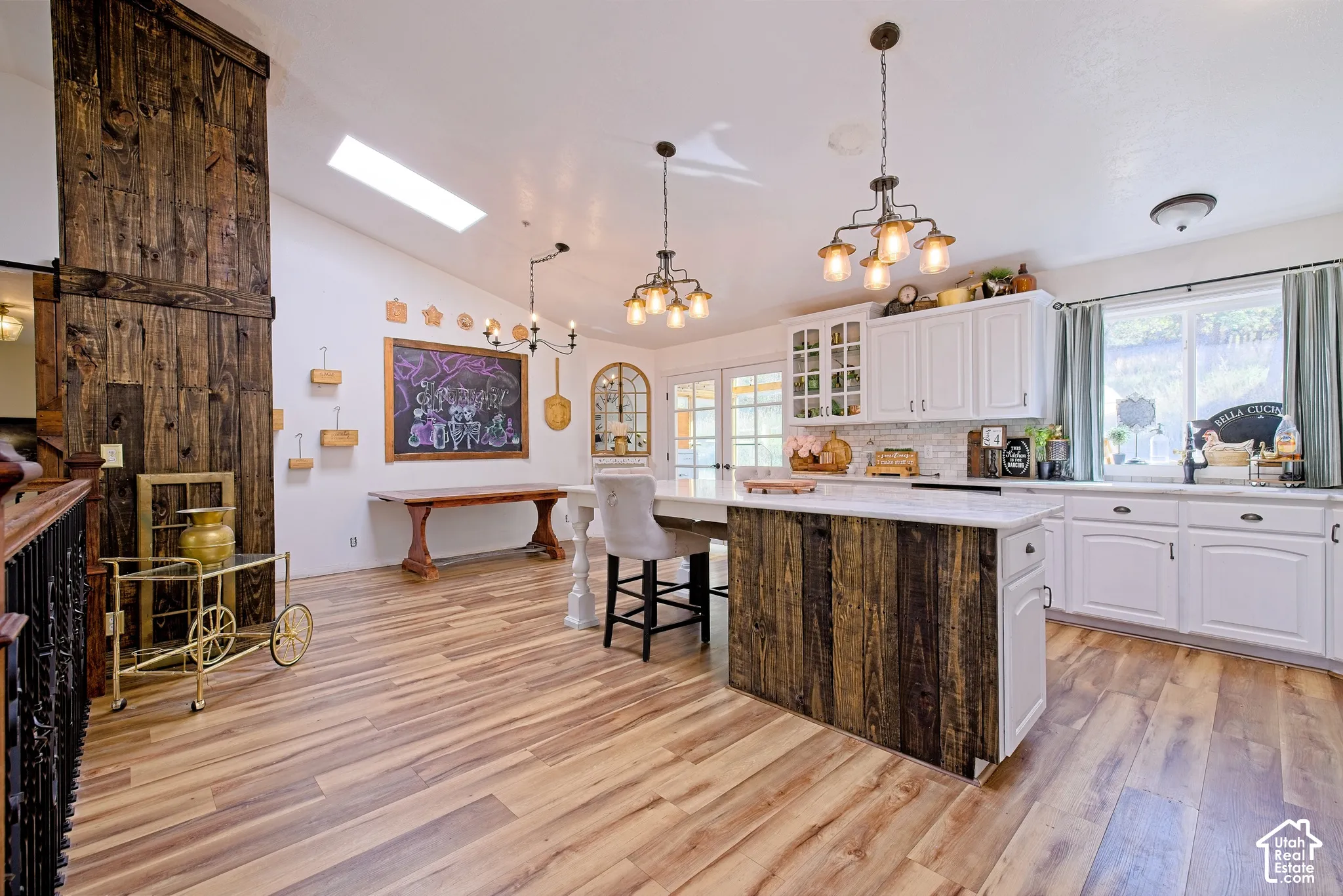 Wood-finish flooring throughout, vaulted ceiling with skylight, white kitchen cabinetry with built-in glass display, center island with wood-panel base, and a large barn door feature