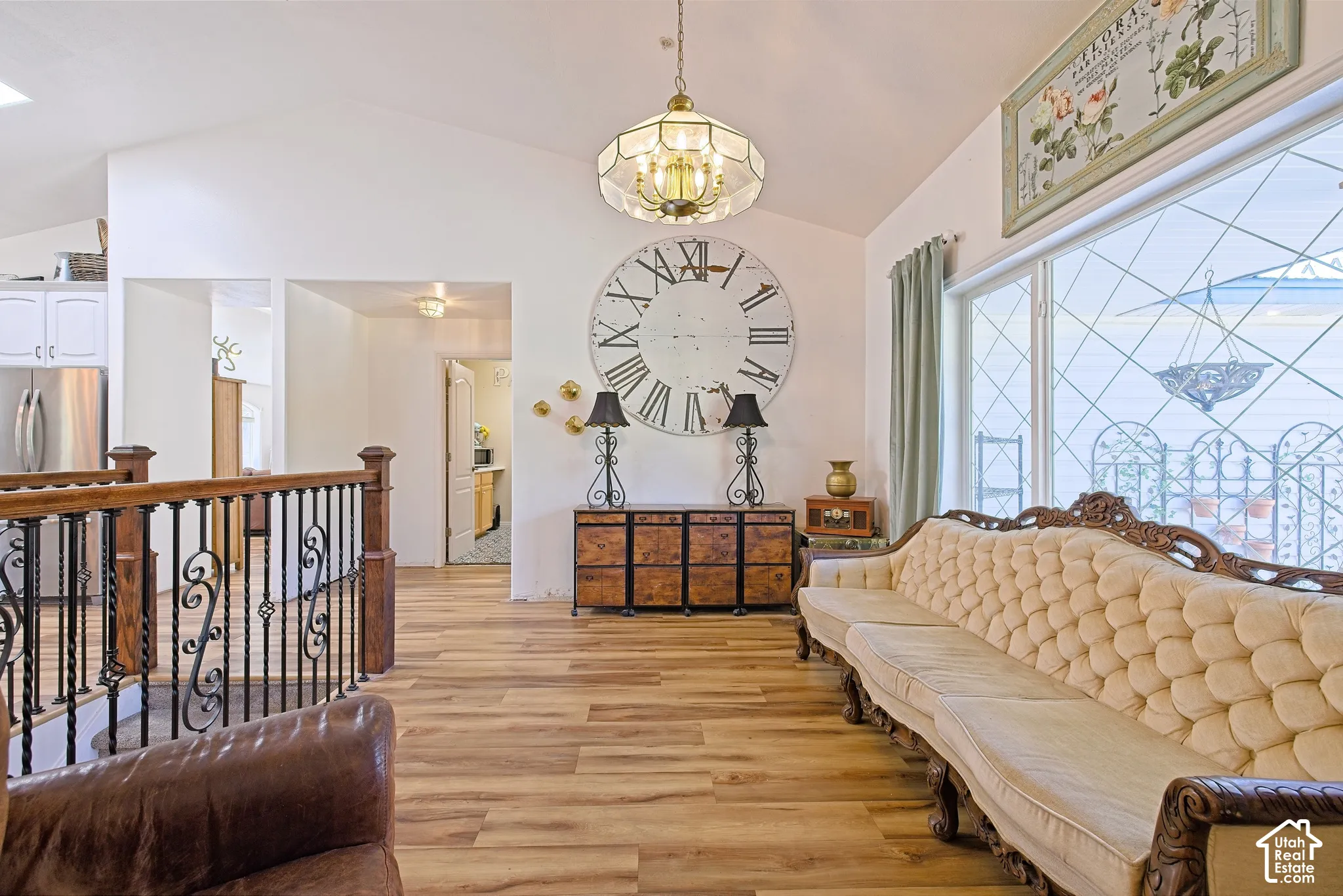 Vaulted ceiling with a decorative chandelier, large window with geometric grilles, wood-finish flooring, and a detailed metal and wood railing