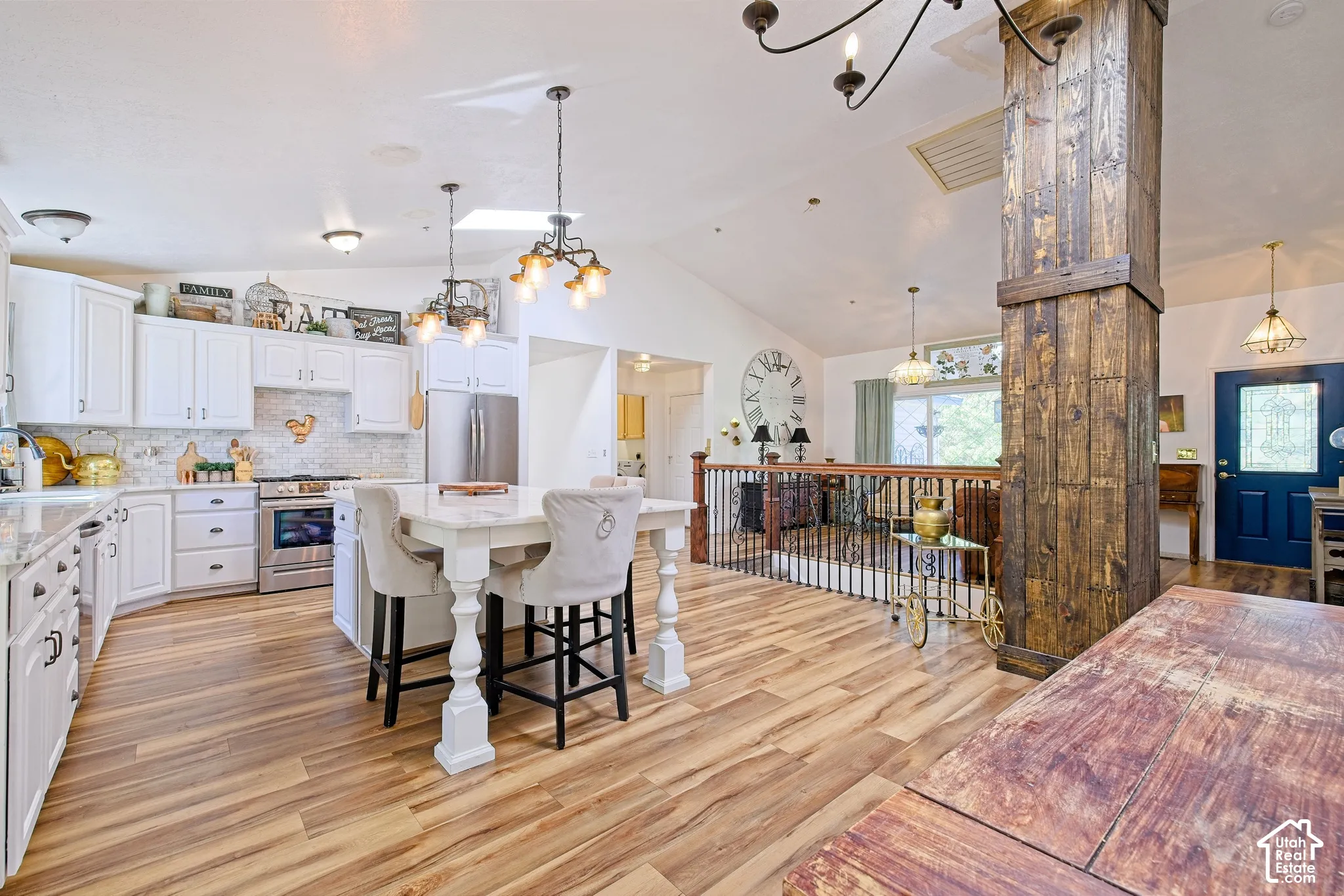 White cabinetry kitchen with stainless steel appliances, central island with seating, wood-finish flooring, and vaulted ceiling