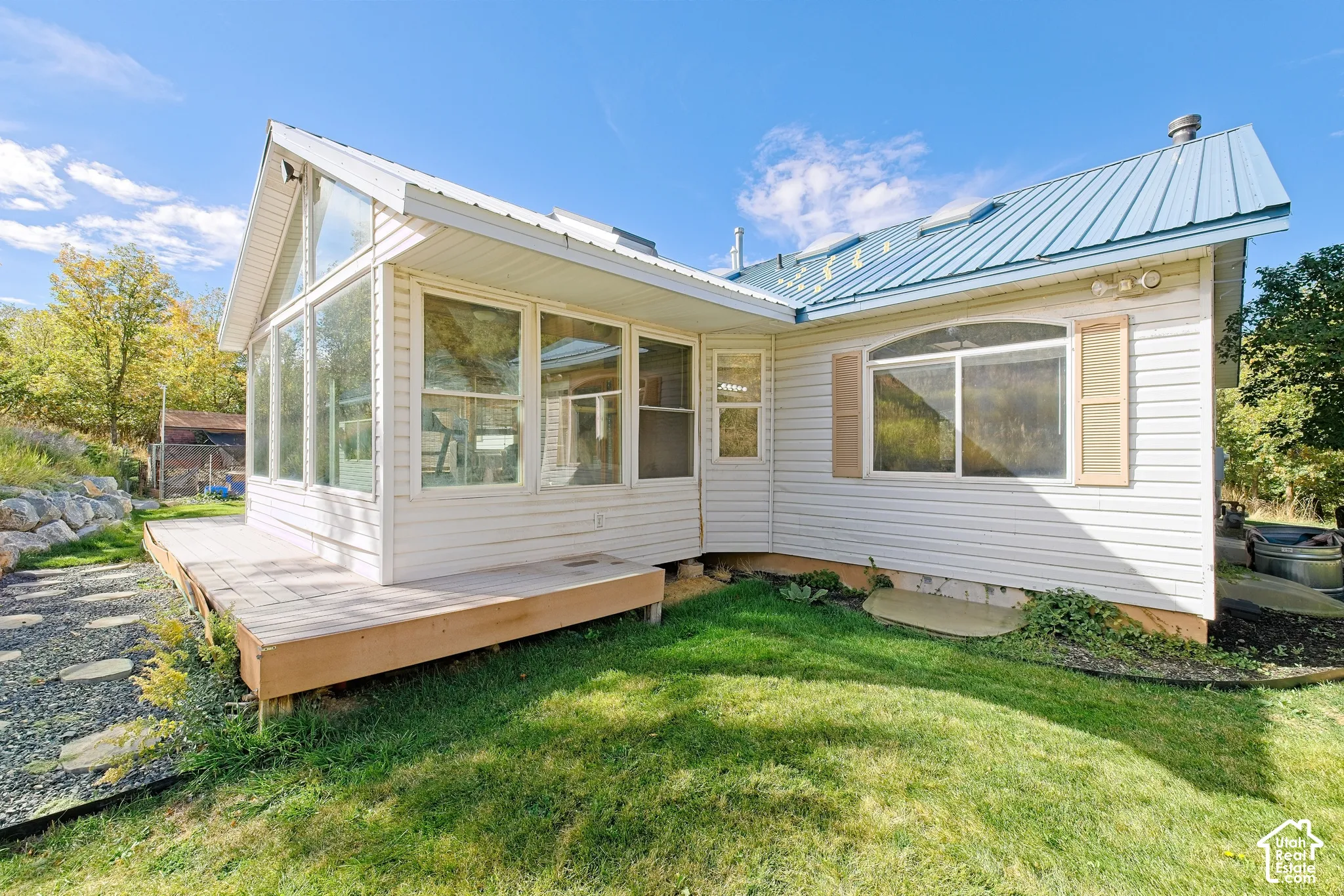 White siding exterior with a blue metal roof, full-light sunroom addition, wood deck, and a grass lawn
