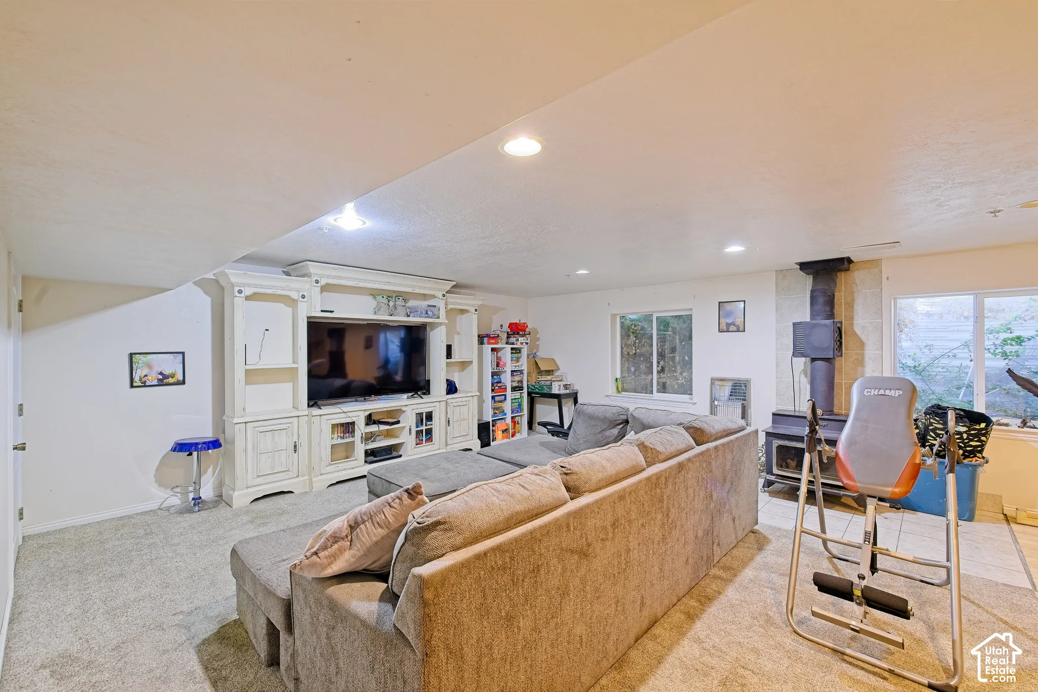 Carpeted living area featuring a built-in media console, recessed lighting, and a wood-burning stove with a flue