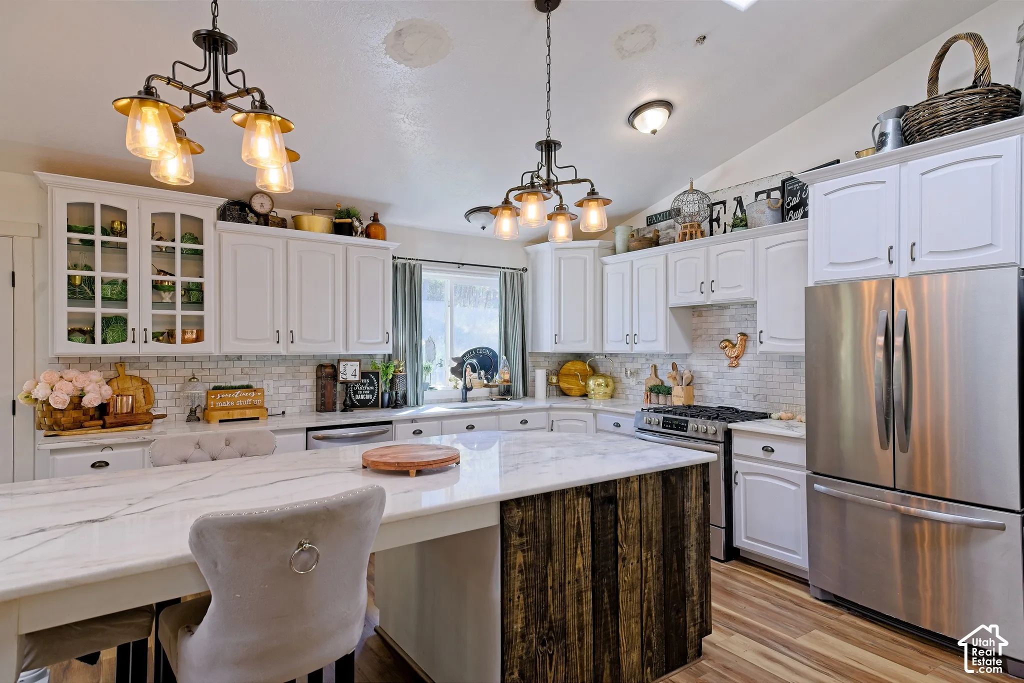 Kitchen featuring white cabinetry, stainless steel appliances, a center island with a wood-finish base, marble-look countertops, and industrial-style pendant lighting