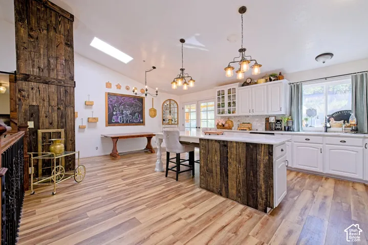 Wood-finish flooring throughout, vaulted ceiling with skylight, white kitchen cabinetry with built-in glass display, center island with wood-panel base, and a large barn door feature
