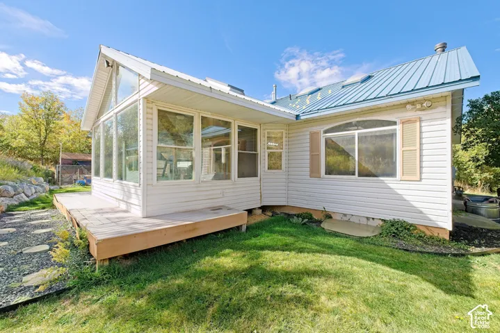 White siding exterior with a blue metal roof, full-light sunroom addition, wood deck, and a grass lawn