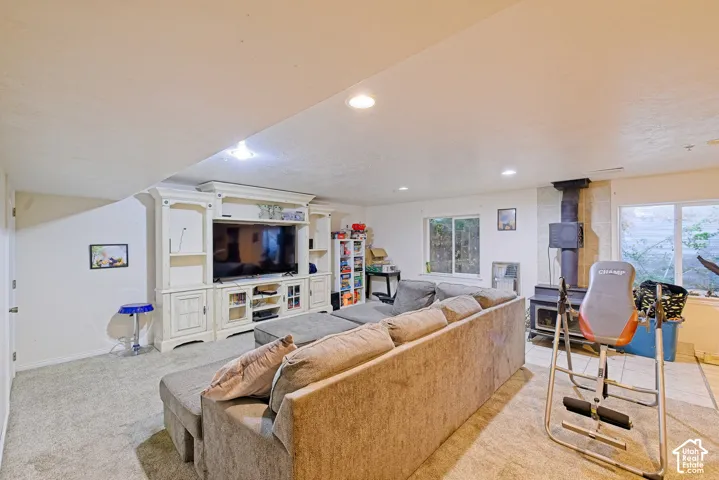 Carpeted living area featuring a built-in media console, recessed lighting, and a wood-burning stove with a flue