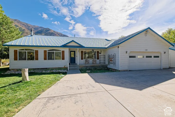 White siding exterior with a blue metal roof, front porch, attached garage, and mountain backdrop