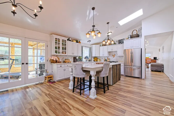 Kitchen featuring wood-finish flooring, white cabinetry, a central island with seating, a skylight, and stainless steel appliances