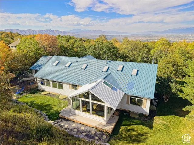 Metal roof with multiple skylights, extensive window line, sunroom with large glass panels, wood deck, and tiered landscaping