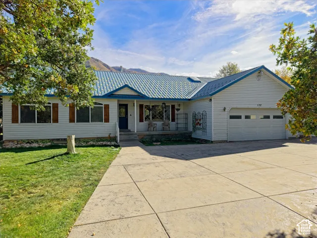White siding exterior with a blue metal roof, an attached garage, a concrete driveway, and a front porch