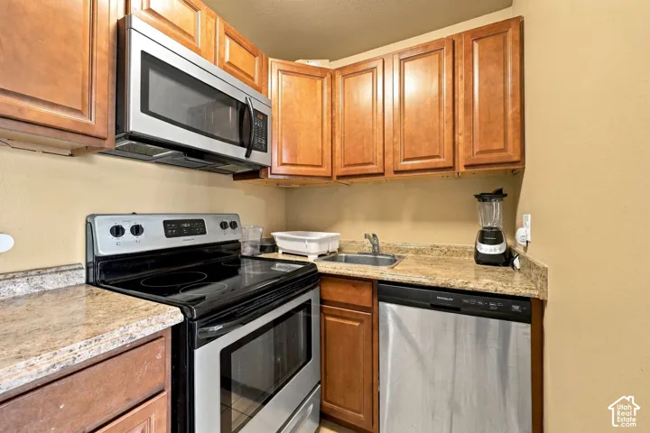 Kitchen featuring wood cabinetry, stainless steel microwave, stainless steel range, stainless steel dishwasher, and stone-finish countertops