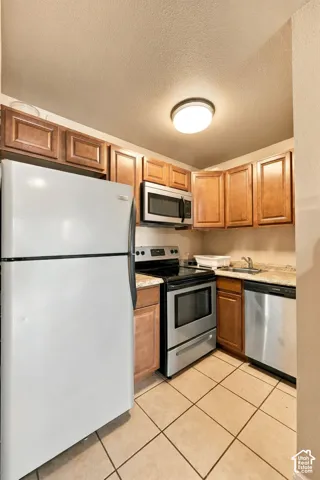 Kitchen featuring wood-finish cabinetry, stainless steel appliances, speckled countertops, and tile flooring