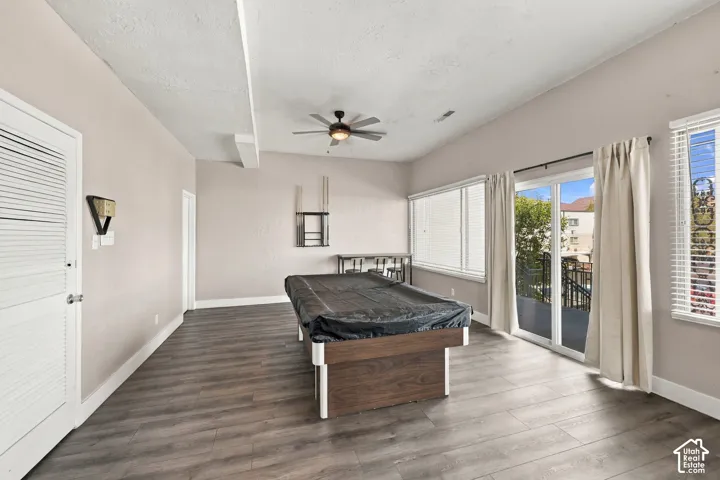 Vaulted ceiling with exposed beam, wood-finish flooring, sliding glass door to exterior, multiple windows, and ceiling fan