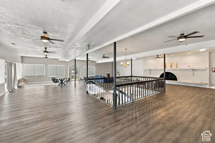 Expansive open floor plan featuring wood-finish flooring, multiple ceiling fans, and a white brick fireplace