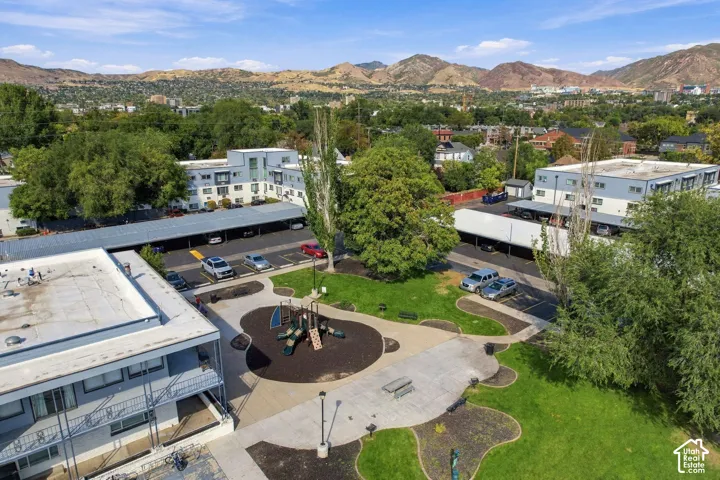 Expansive central green space with a dedicated playground area, mature trees, paved walkways, and covered parking structures