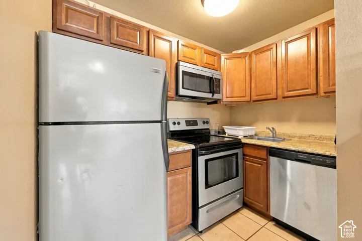 Kitchen featuring wood-finish cabinetry, stainless steel microwave, stainless steel range, stainless steel dishwasher, and a stone-finish countertop