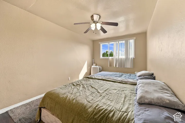Wood-finish flooring with an area rug, a ceiling fan with integrated lighting, and a window featuring vertical blinds
