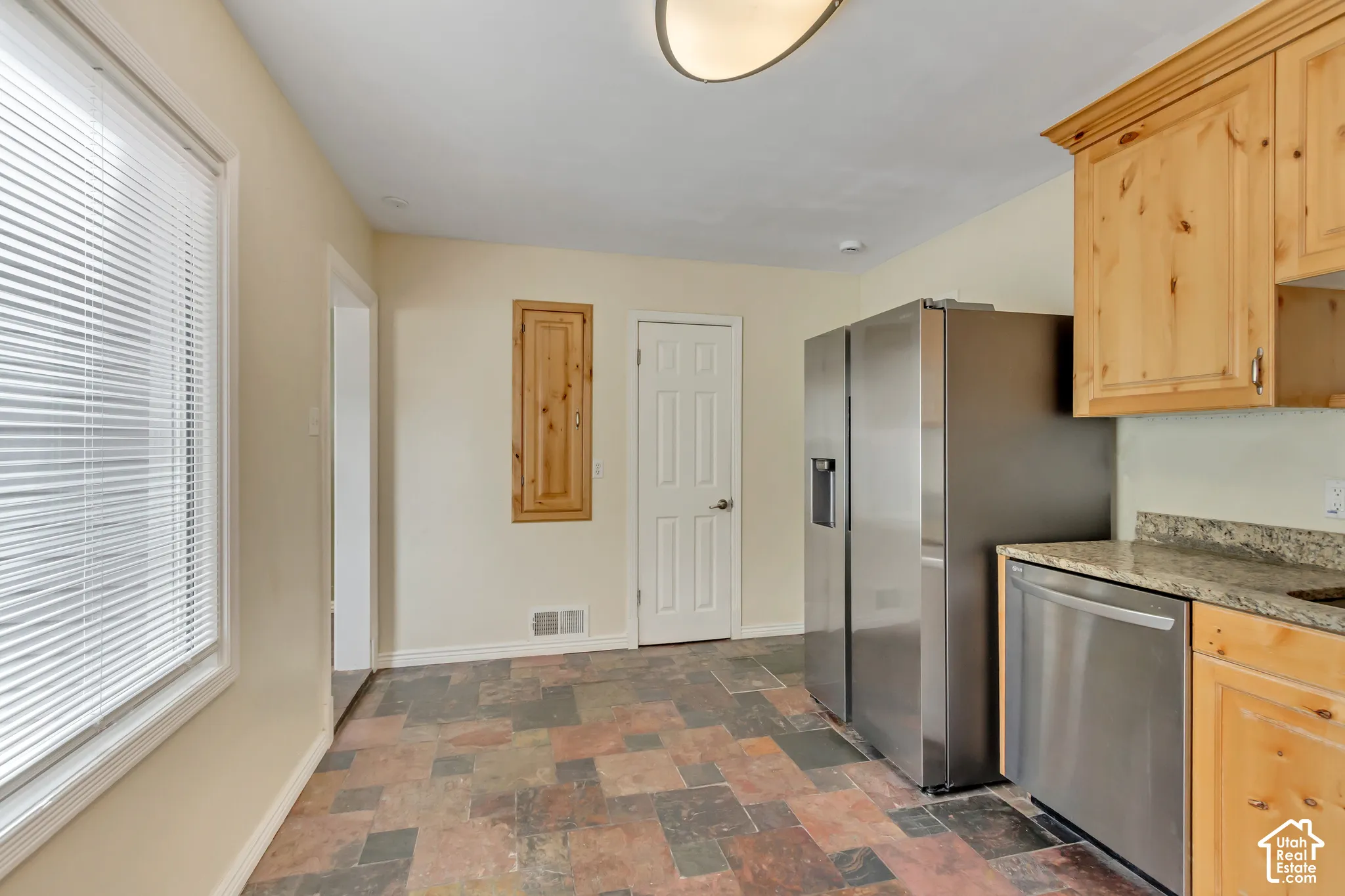Stainless steel French door refrigerator, stainless steel dishwasher, light wood-finish cabinetry, stone-finish countertops, and multi-tone tile flooring