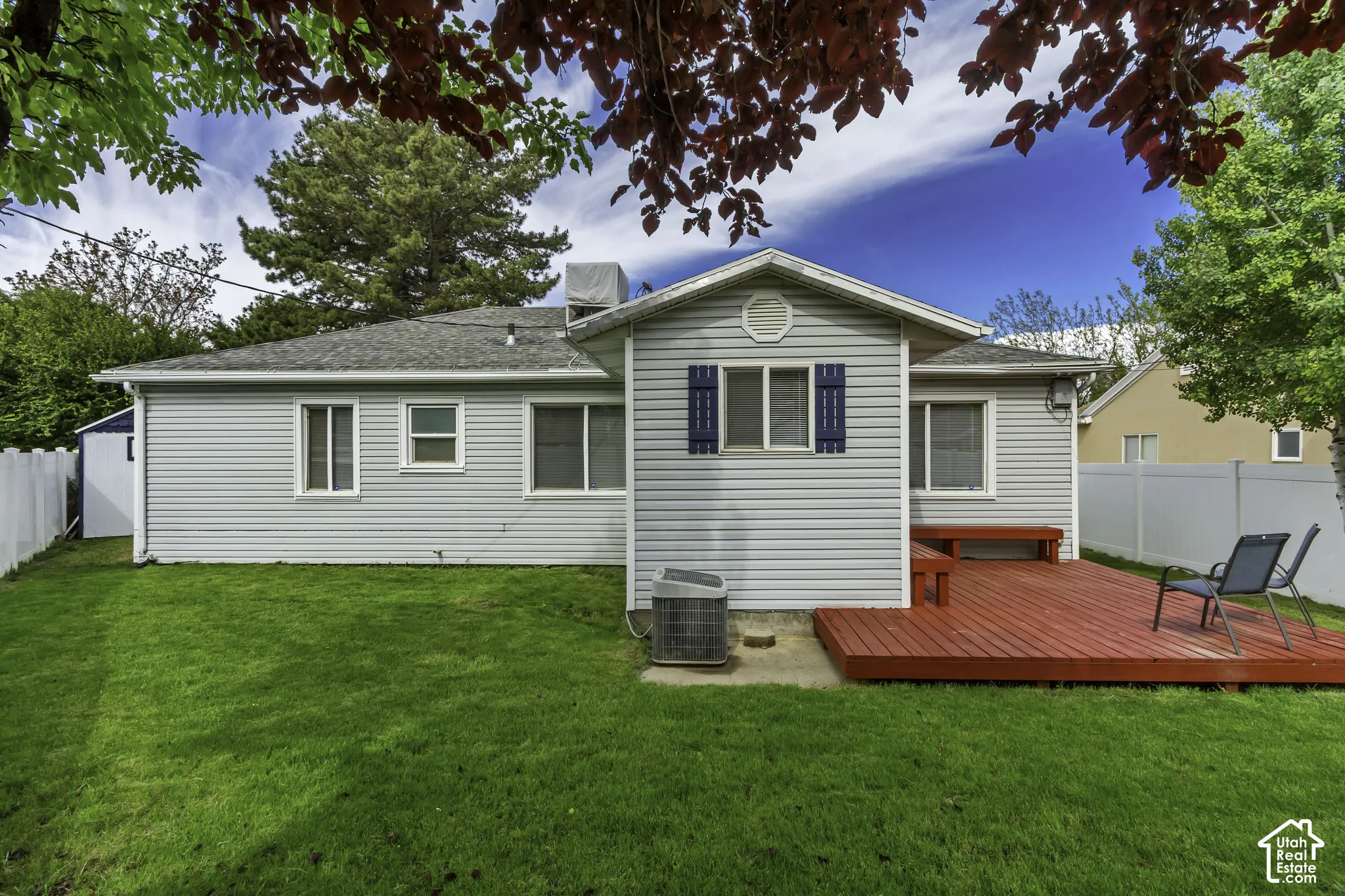 Expansive green lawn, red wood-finish deck, exterior siding, multiple windows, and a white privacy fence