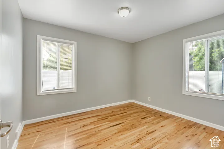 Light wood-finish flooring, two windows with white blinds, and a semi-flush mount ceiling light fixture