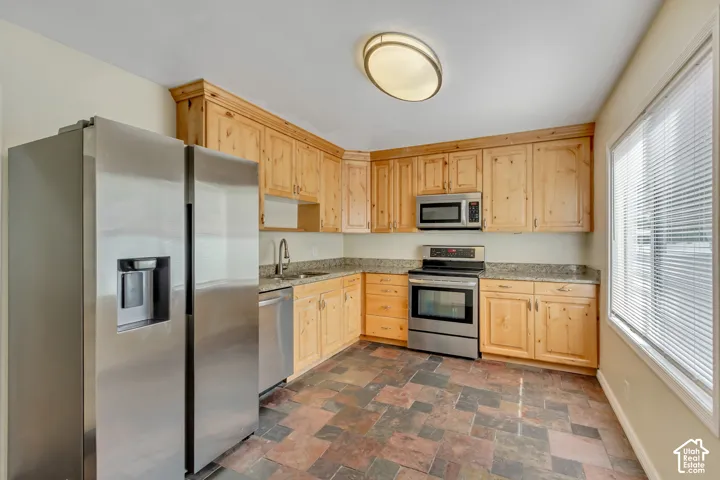 Kitchen featuring stainless steel appliances, wood cabinetry, granite countertops, and slate-style floor tiling