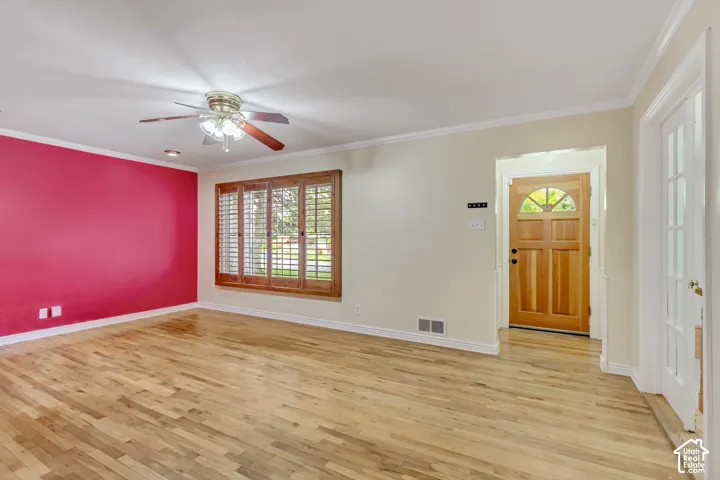 Wood-finish flooring, ceiling fan with light fixture, decorative wood window shutters, crown molding, and a wood entry door with a decorative glass insert