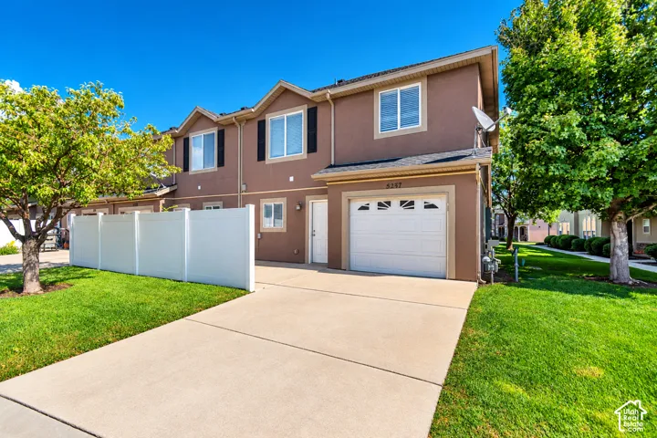 Two-story townhome with stucco exterior, attached garage, concrete driveway, and a white privacy fence