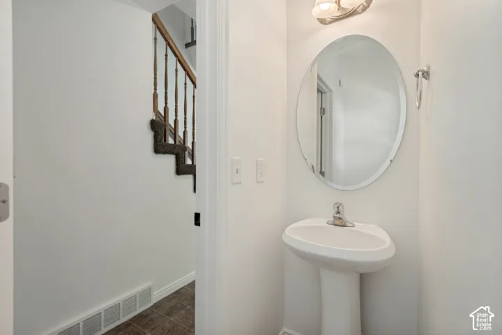 Pedestal sink with a polished chrome faucet, oval mirror, and wall-mounted vanity lighting