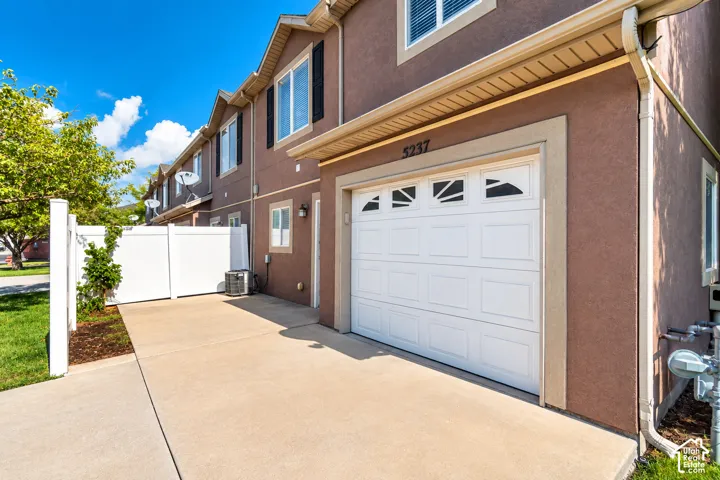 Exterior featuring a stucco finish, white paneled garage door with decorative windows, concrete driveway, and white privacy fencing