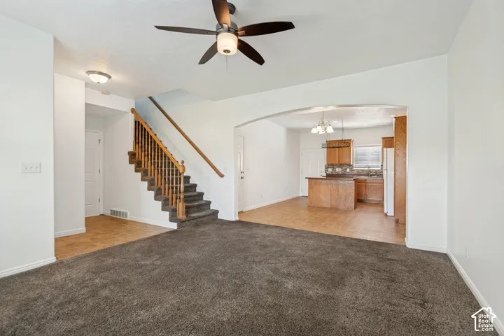 Open concept living space with a ceiling fan, arched doorway, wood-finish cabinetry, and a kitchen island