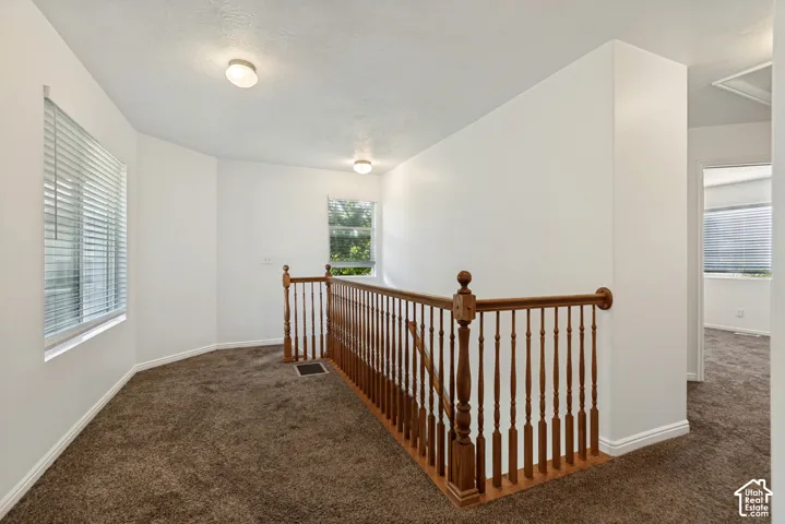 Spacious upper-level landing featuring rich wood railings with turned balusters, recessed ceiling lighting, neutral wall finishes, and plush carpeting throughout