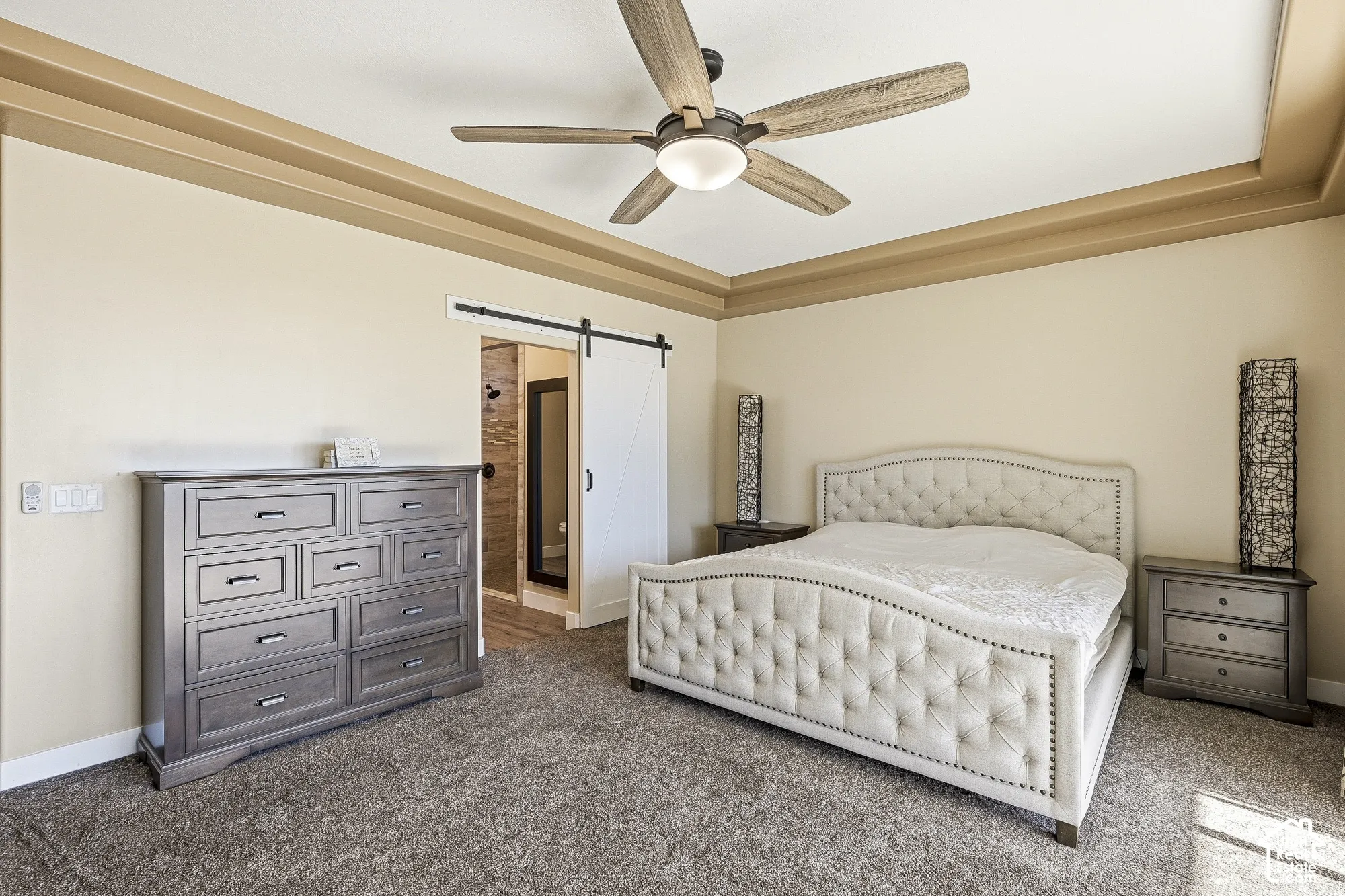 Tray ceiling with crown molding, ceiling fan with light fixture, carpeted flooring, and barn door entry