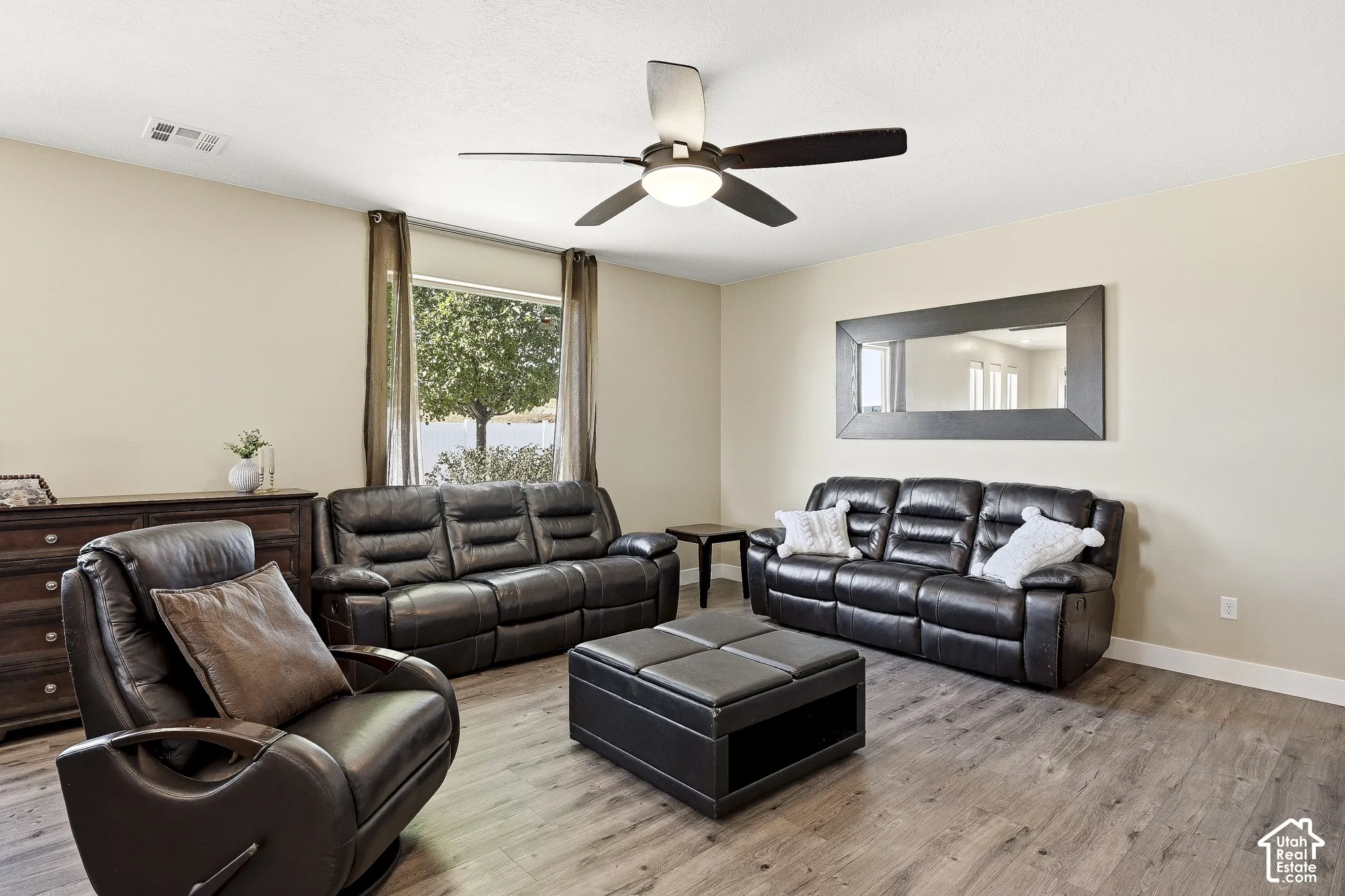Wood-finish flooring throughout, ceiling fan with integrated lighting, and a large window with outdoor scenery