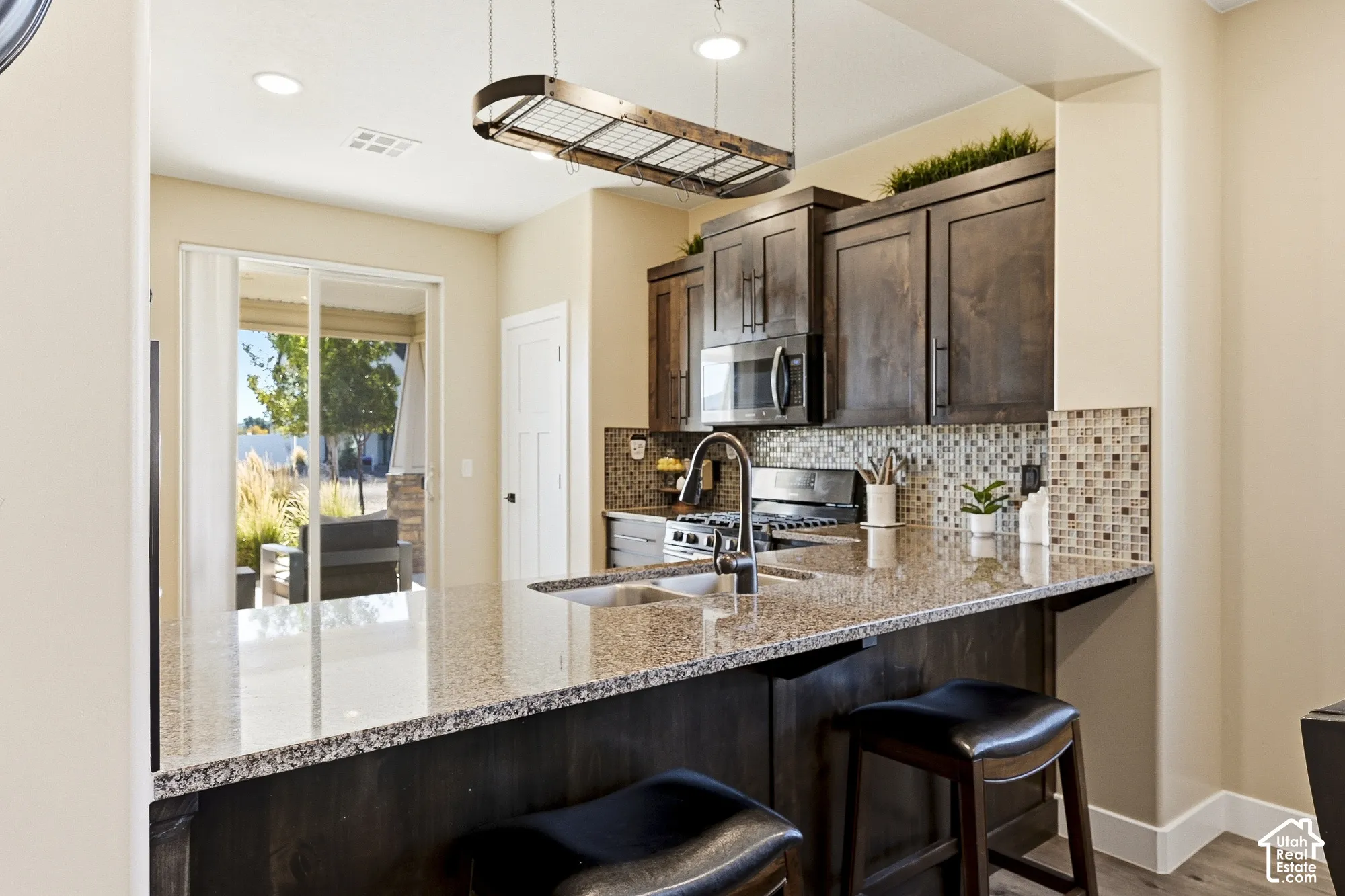 Granite countertops with an undermount sink, dark wood-finish cabinetry, stainless steel appliances, mosaic tile backsplash, and a sliding glass door