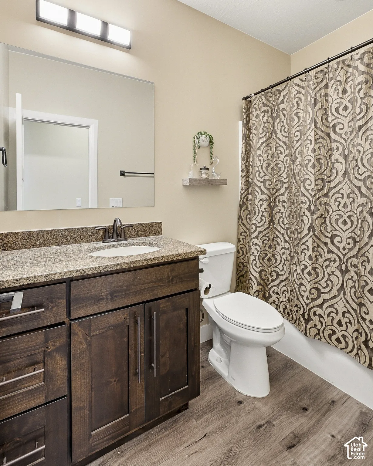 Bathroom featuring a dark wood-finish vanity with an undermount sink, a speckled countertop, and wood-finish flooring