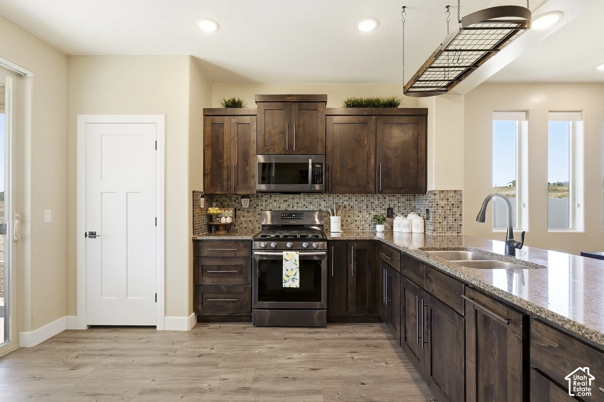 Kitchen featuring wood-finish flooring, dark wood cabinetry, stainless steel appliances, speckled countertops, and a mosaic tile backsplash