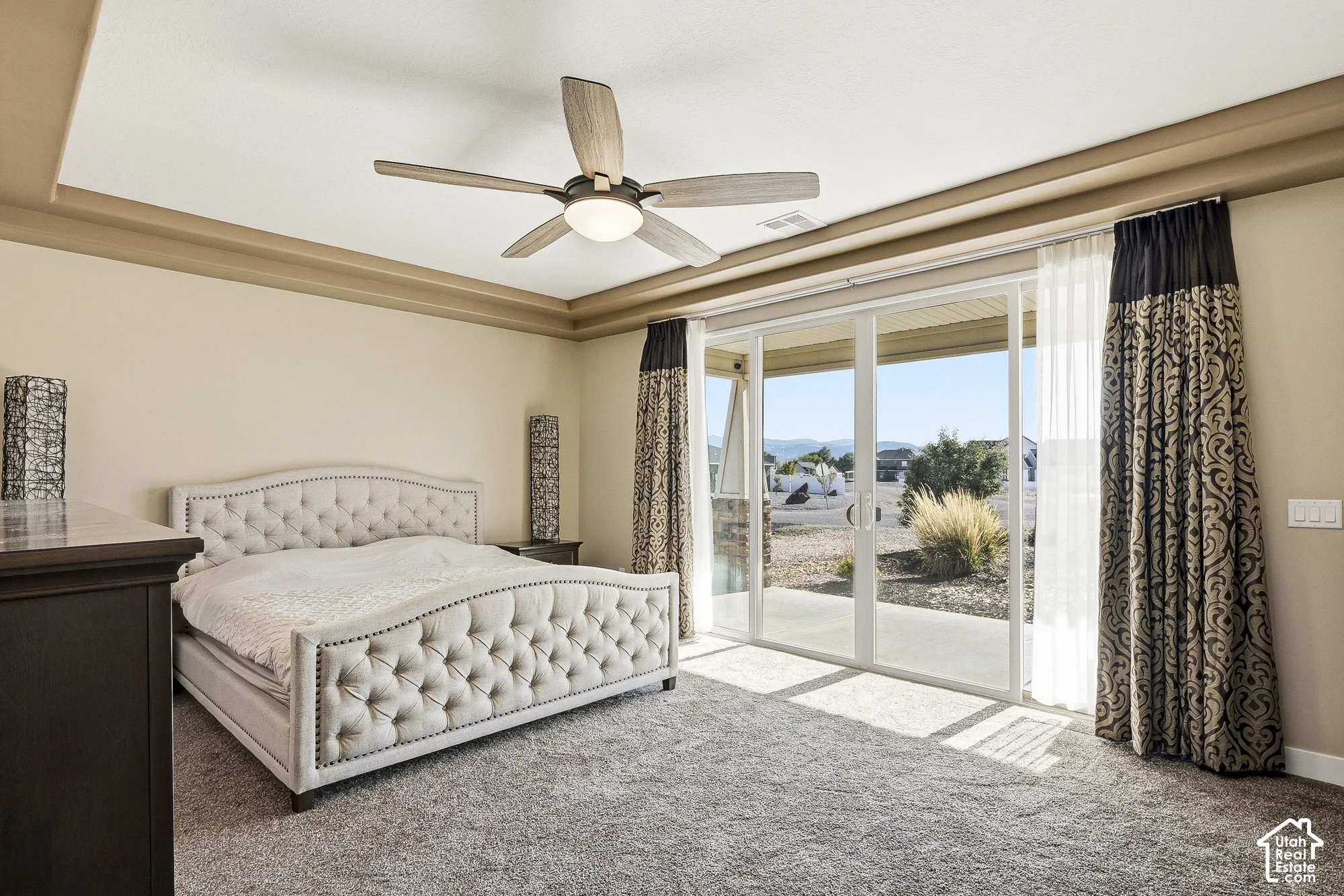 Tray ceiling with crown molding, ceiling fan, sliding glass doors, and patterned drapery
