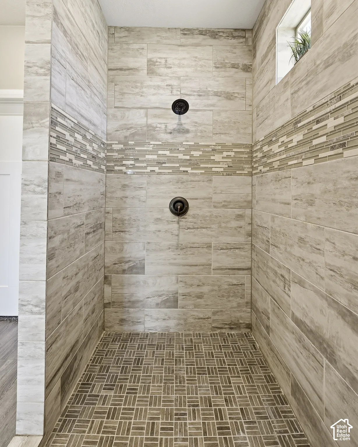 Tiled shower stall with dual shower heads, horizontal mosaic tile accent, and a built-in window