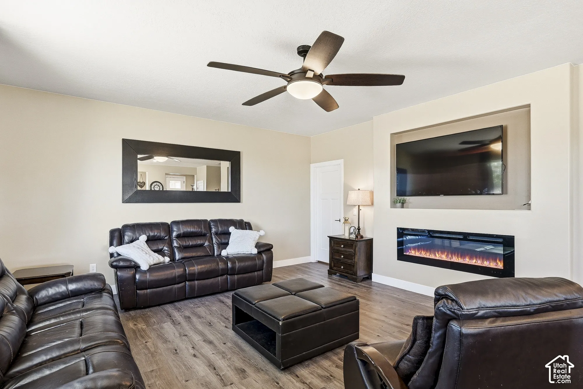Wood-finish flooring, built-in entertainment niche, integrated linear fireplace, and ceiling fan with integrated lighting