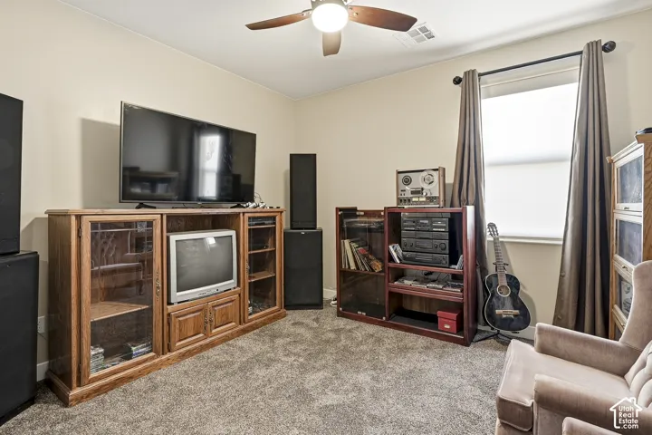 Textured carpet flooring, ceiling fan with light fixture, window with roller shade and curtains, and neutral wall paint
