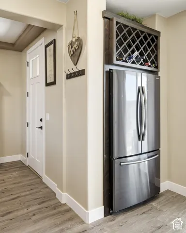 Stainless steel French-door refrigerator, integrated wooden wine rack, wood-finish flooring, white trim, and a white paneled door