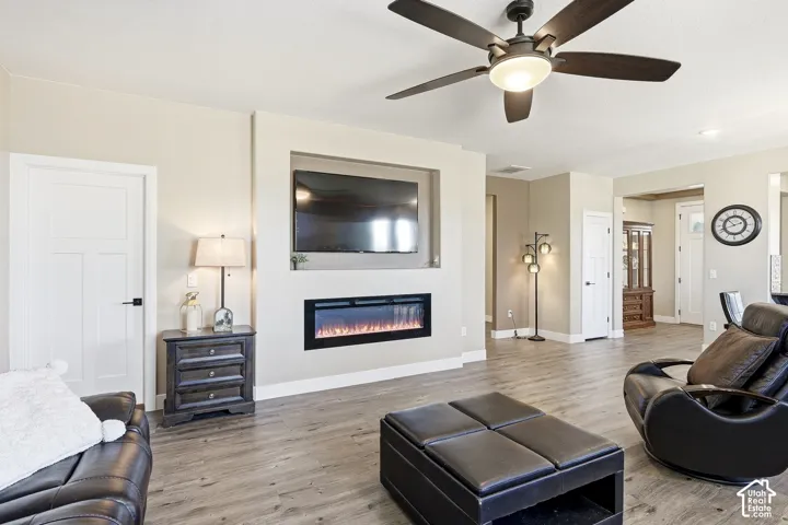 Wood-finish flooring, recessed electric fireplace, built-in media niche, ceiling fan with integrated lighting, and white paneled doors